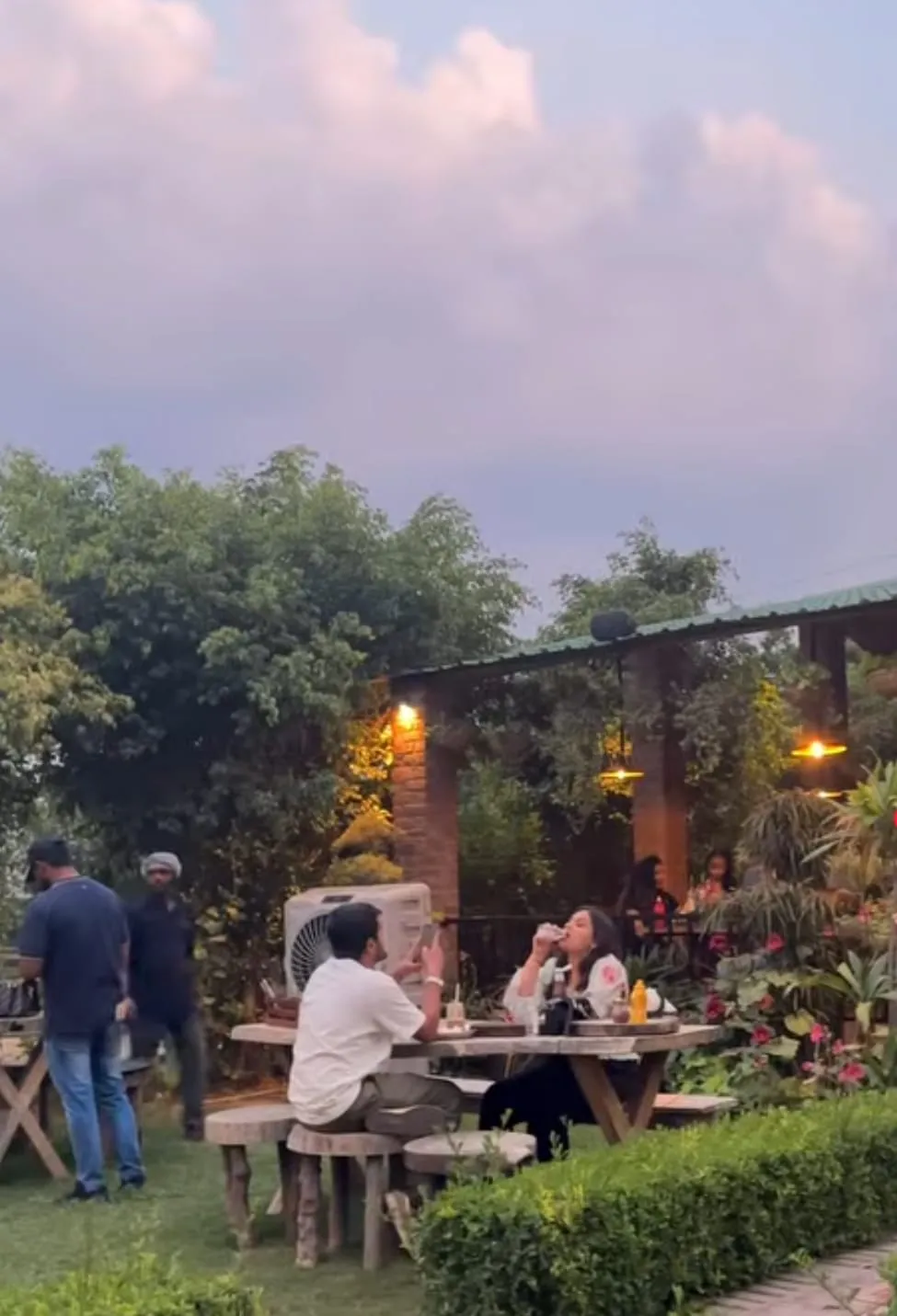 Diners at Caffe Cavallo at dusk, warm pendant lights overhead and sunset clouds above the garden seating.