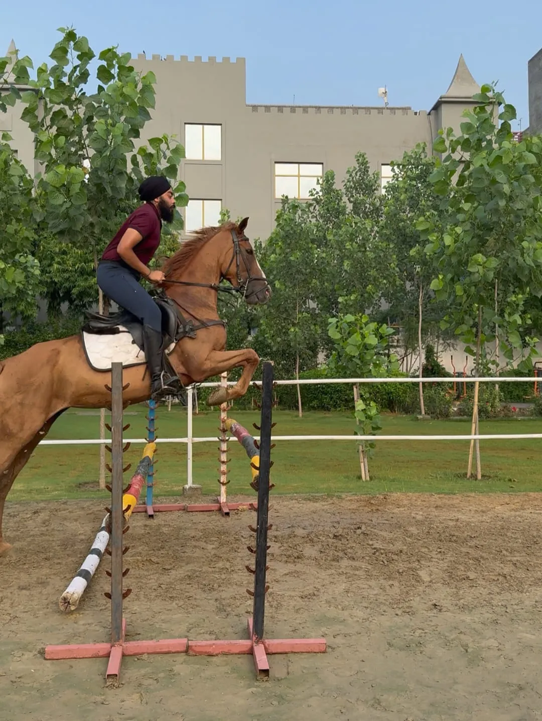 A chestnut horse and rider mid-jump over a fence in the FHRC arena at evening light.
